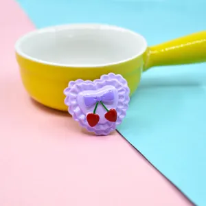 Detailed macro shot of a purple heart resin charm with bow and red cherry accents.