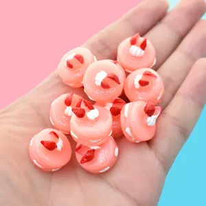 Detailed macro view of pink strawberry cake resin charms held in hand for DIY crafts