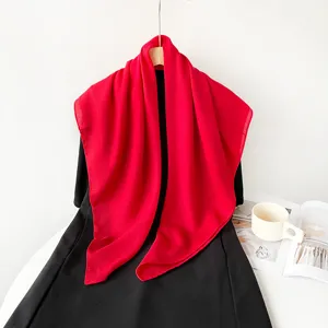 Detail shot of solid red square scarf draped on black fabric, soft lightweight fabric headscarf.