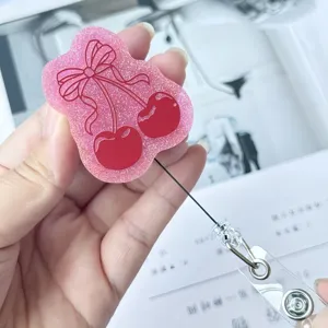 Détail d'un porte-badge rétractable en acrylique pailleté rose au motif de cerise mignon.