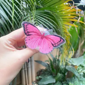 Close-up detail of a vibrant pink butterfly acrylic phone grip held in hand outdoors