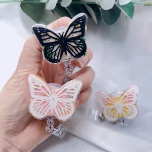 Close-up of hand holding three butterfly resin badge reels with real flowers and gold foil.