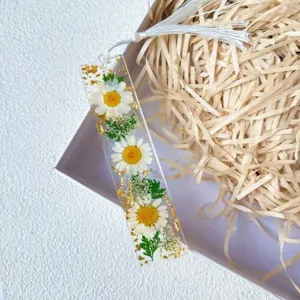Close-up of a resin bookmark with real dried daisies, green leaves, and gold foil