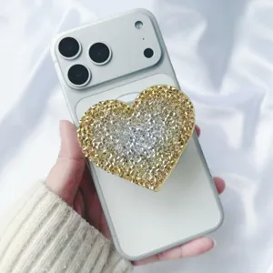 Close-up of a heart-shaped sparkling rhinestone phone grip on a white smartphone