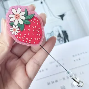 Détail d'un joli porte-badge rétractable en forme de fraise rose pailletée dans la main
