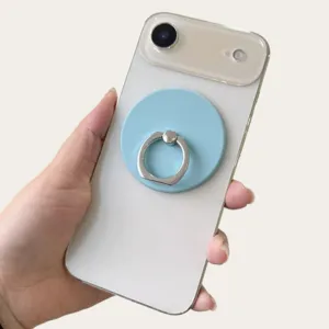 Light blue magnetic ring holder attached to a white smartphone back, held in a hand