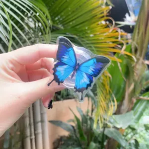 Detail showing a blue butterfly acrylic phone grip held against a tropical green plant background