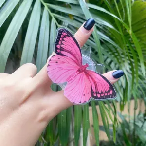 Detailed view of a pink butterfly acrylic phone grip stand held on a hand with blue nails