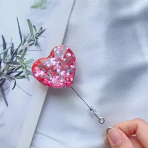 Detailansicht eines glitzernden Herz-Ausweishalters mit ausziehbarer Kordel in der Hand
