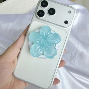 Nahaufnahme eines hellblauen 3D-Glitzer-Blumen-Handyhalters aus Harz auf weißem Handy