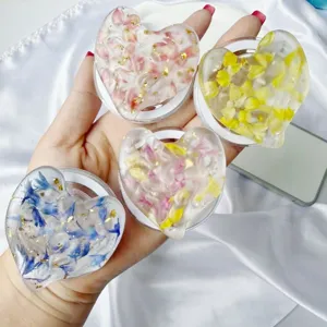 Macro view of four heart-shaped resin phone grips with real dried flowers and gold foil.
