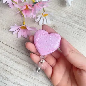Nahaufnahme eines funkelnden rosa herzförmigen Glitzer-Ausweishalters in der Hand