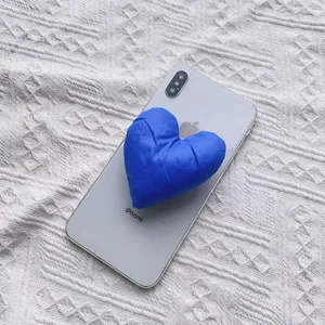 Detailaufnahme eines blauen, gepolsterten Herz-Handyhalters aus Stoff auf einem Handy