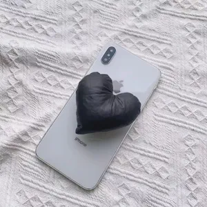 Nahaufnahme einer schwarzen Herz-Handyhalterung aus Stoff auf einem weißen Smartphone