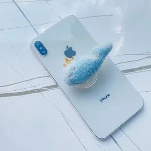 Détail d'un support de téléphone baleine en peluche bleue sur smartphone blanc