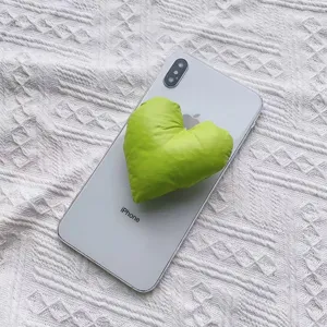 Nahaufnahme einer grünen herzförmigen Handyhalterung aus Stoff am Smartphone.