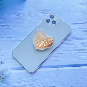 Nahaufnahme einer herzförmigen Quicksand-Handyhalterung mit goldenem Glitzer auf einem Handy