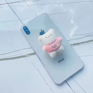 Gros plan d'un support de téléphone en peluche d'ours blanc avec pull rose sur mobile