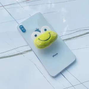 Détail d'un support de téléphone en peluche grenouille verte sur un smartphone blanc