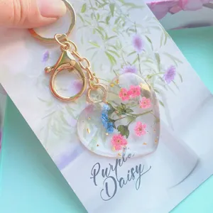 Detailed close-up of heart resin keychain with pink dried flowers and gold flakes