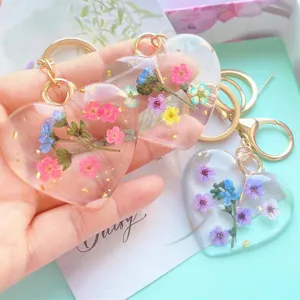 Close-up of heart-shaped resin keychains featuring real dried flowers and gold leaf accents.