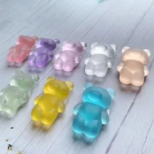 Variety of colorful translucent frosted bear-shaped phone grips on wooden surface.
