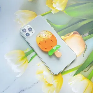Detailopname van een oranje ijsje-vormige telefoonhouder op een witte smartphone.