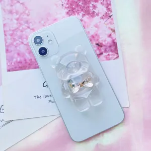 Dettaglio di un supporto per telefono a forma di orso in resina con fiocco dorato.