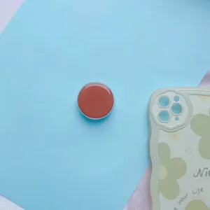 Close-up van een ronde terracotta epoxy telefoonhouder op een lichtblauwe achtergrond