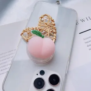 Close-up of a 3D pink peach squishy phone grip holder on a clear iPhone case background