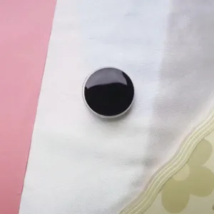 Close-up van een glanzend zwarte ronde telefoonhouder op een zachte, getextureerde achtergrond