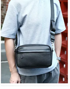 Men's leather messenger bag detail, showing pebbled texture and black shoulder strap.
