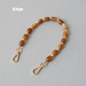 Détail d'une bandoulière en perles acryliques caramel de 37 cm avec fermoirs dorés.