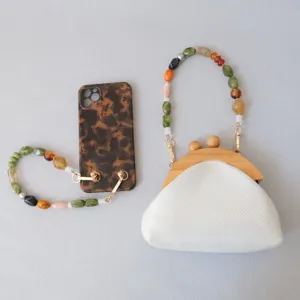 Gros plan d'une pochette blanche avec des lanières en perles acryliques et une chaîne de téléphone.