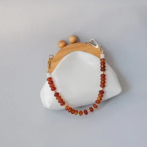 Gros plan d'une chaîne de sac en perles acryliques sur une pochette blanche épurée