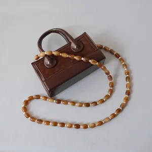 Gros plan d'une bandoulière en chaîne de perles en acrylique caramel sur un sac à main brun