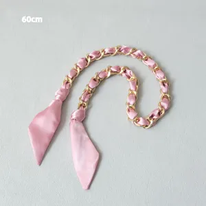 Détail d'une bandoulière de 60 cm en soie satinée rose entrelacée d'une chaîne en métal doré.