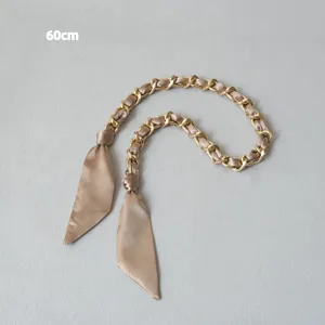 Gros plan d'une chaîne dorée élégante entrelacée d'un foulard en soie champagne.
