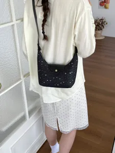 Détail d'un sac hobo croissant noir chic avec motif d'étoiles porté par un modèle