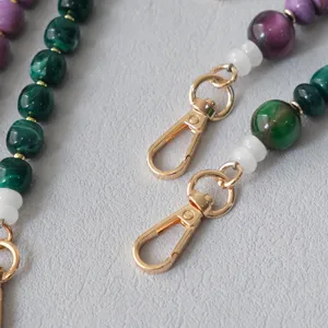 Dettaglio di perline in acrilico marmorizzato e moschettoni dorati su una tracolla trendy