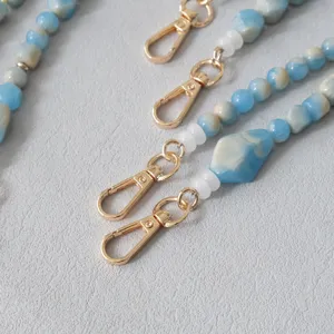 Dettaglio ravvicinato della catena in perle acriliche marmorizzate blu con moschettoni dorati