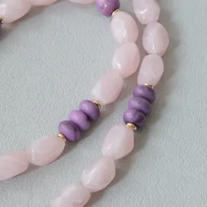 Gros plan d'une chaîne en perles acryliques roses et violettes avec des accents dorés.