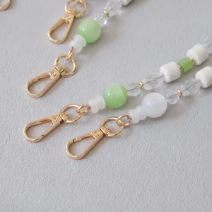 Macro detail of green and white acrylic beaded mobile strap with gold lobster clasps.