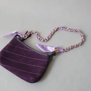 Détail d'un sac à main en velours violet avec chaîne dorée entrelacée de ruban satin violet