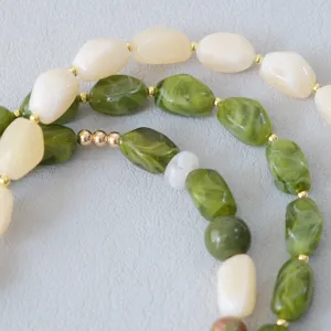 Gedetailleerde macro-opname van gemarmerde groene en crème acryl kralen op een sierlijke ketting