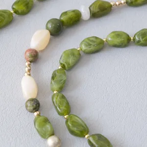 Close-up van groene gemarmerde harskralen met gouden accenten aan een telefooneketting.