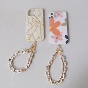 Dettaglio di cover per cellulare con catene in resina beige e metallo dorato alla moda.