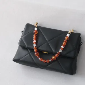 Dettaglio della tracolla decorativa in perle acriliche ambra e bianche su borsa trapuntata