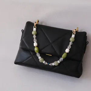 Detailed view of a black quilted purse featuring a green and white resin beaded chain strap