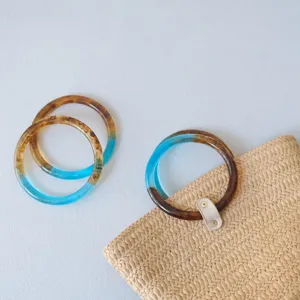 Primer plano de las asas de resina azul y ámbar en un bolso de paja tejido artesanal